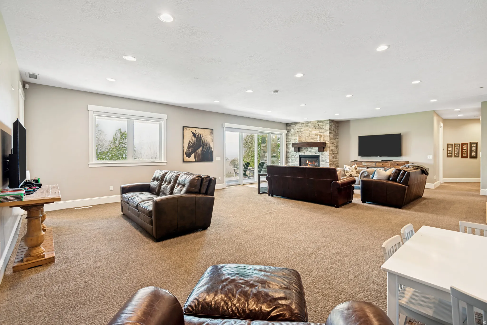 Expansive carpeted living space featuring recessed lighting, a stone-clad fireplace with a wood mantle, and sliding glass doors to the exterior