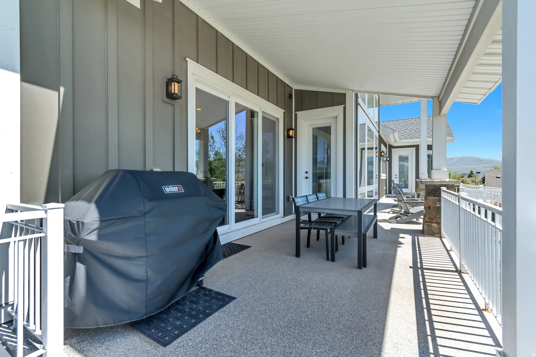 Spacious covered patio featuring textured concrete flooring, white railing, and exterior wall sconces