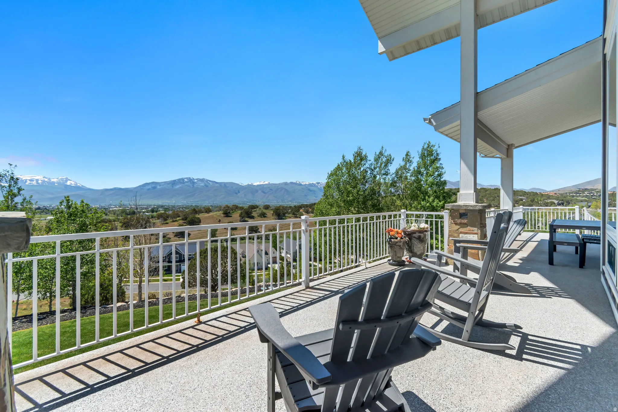 Spacious covered balcony with textured concrete flooring, white metal railing, and stone-clad pillar