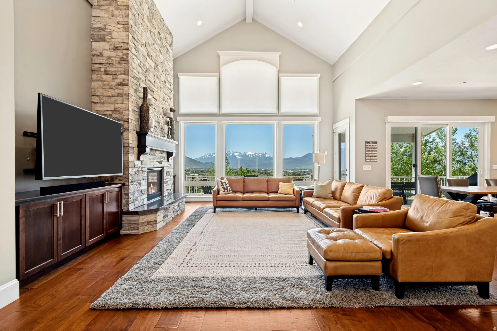 Vaulted ceiling living room featuring a floor-to-ceiling stone fireplace, built-in media cabinetry, wood-finish flooring, and expansive windows
