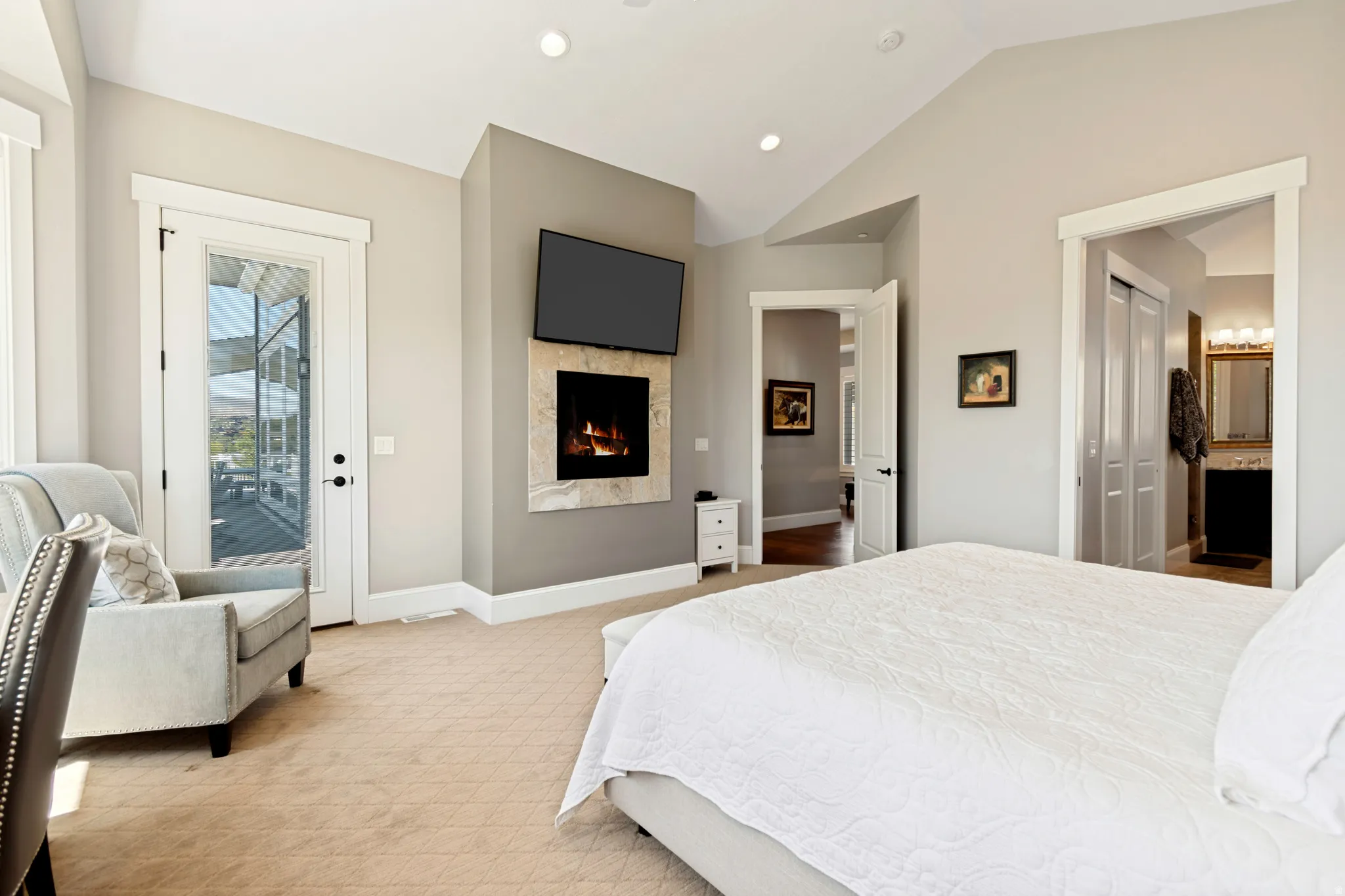 Vaulted ceiling room featuring a gas fireplace with stone surround, a glass-paneled door leading to an outdoor space, and beige patterned carpeting