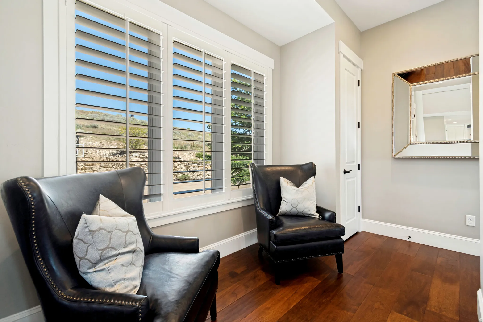 Window wall with white plantation shutters, rich wood-finish flooring, and crisp white trim