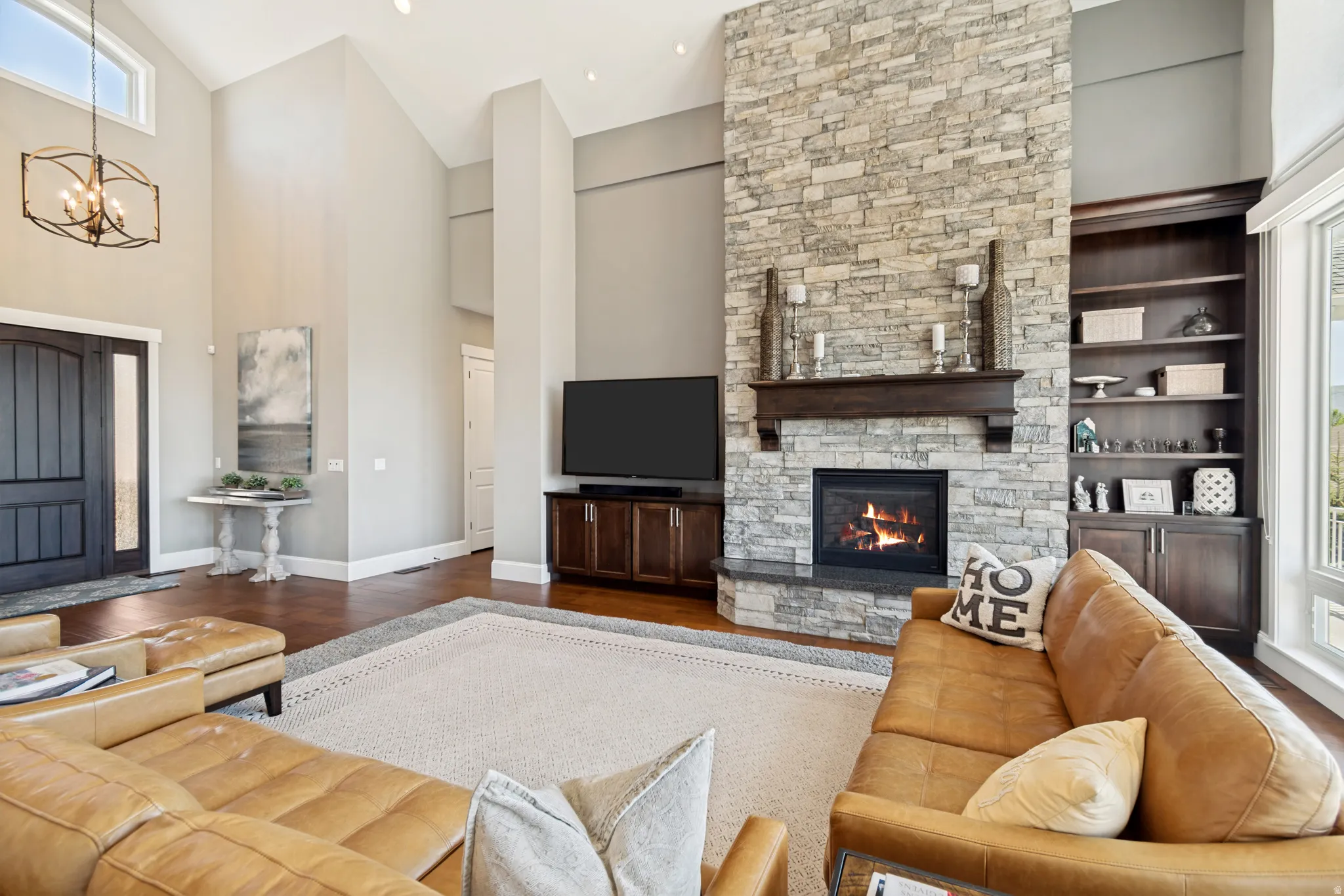 Spacious living area featuring a stone-clad fireplace with wood mantel, built-in shelving, high vaulted ceilings, and wood-finish flooring