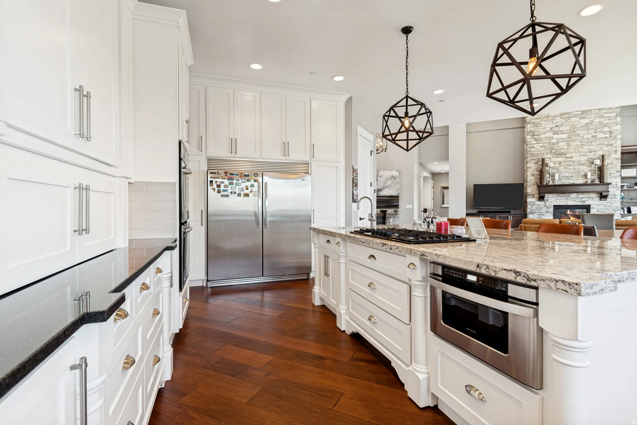 Gourmet kitchen featuring a large central island with a gas cooktop, white cabinetry, integrated stainless steel appliances, dark wood-finish flooring, and pendant lighting