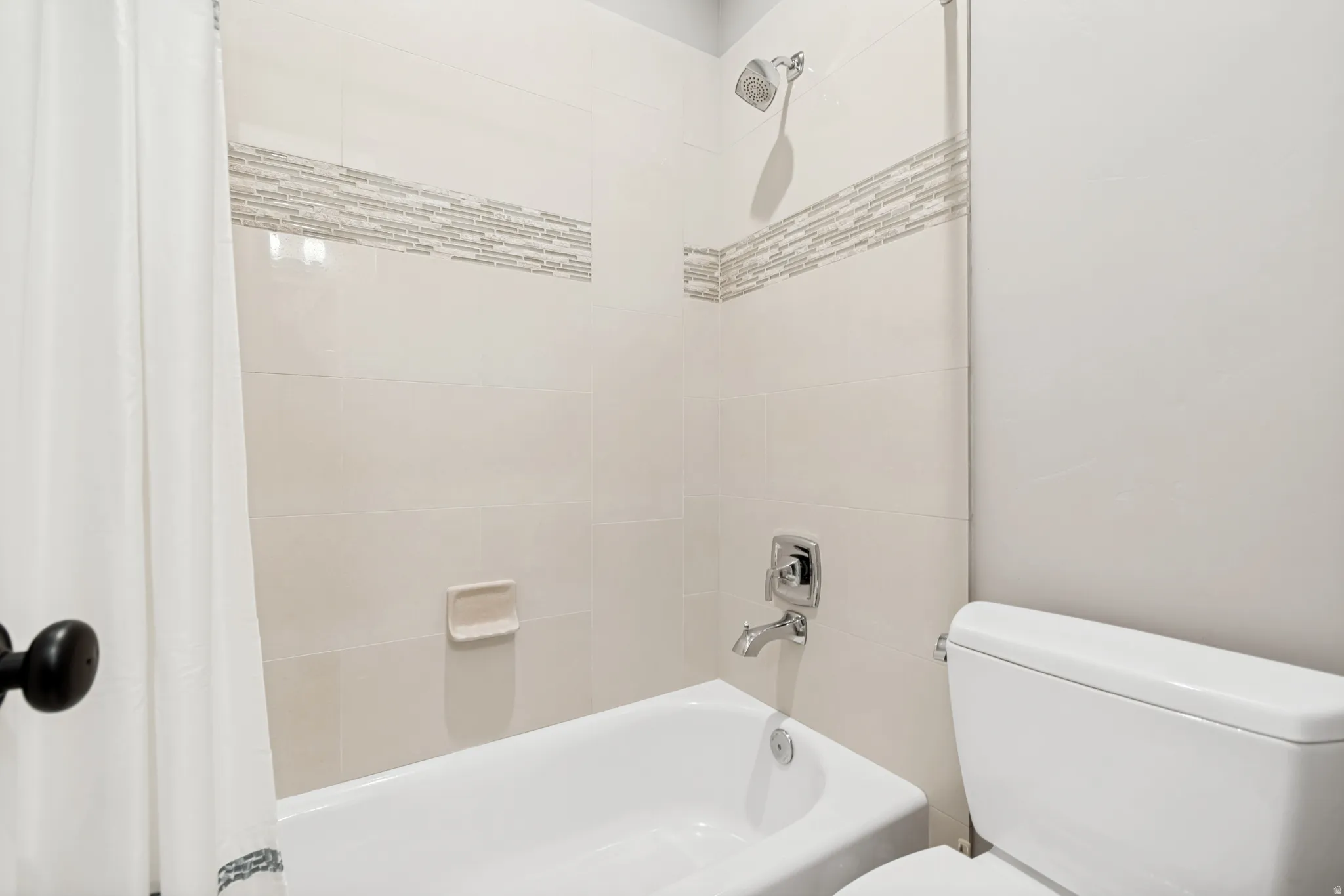 Bathtub with subway tile surround, decorative mosaic accent band, and chrome fixtures