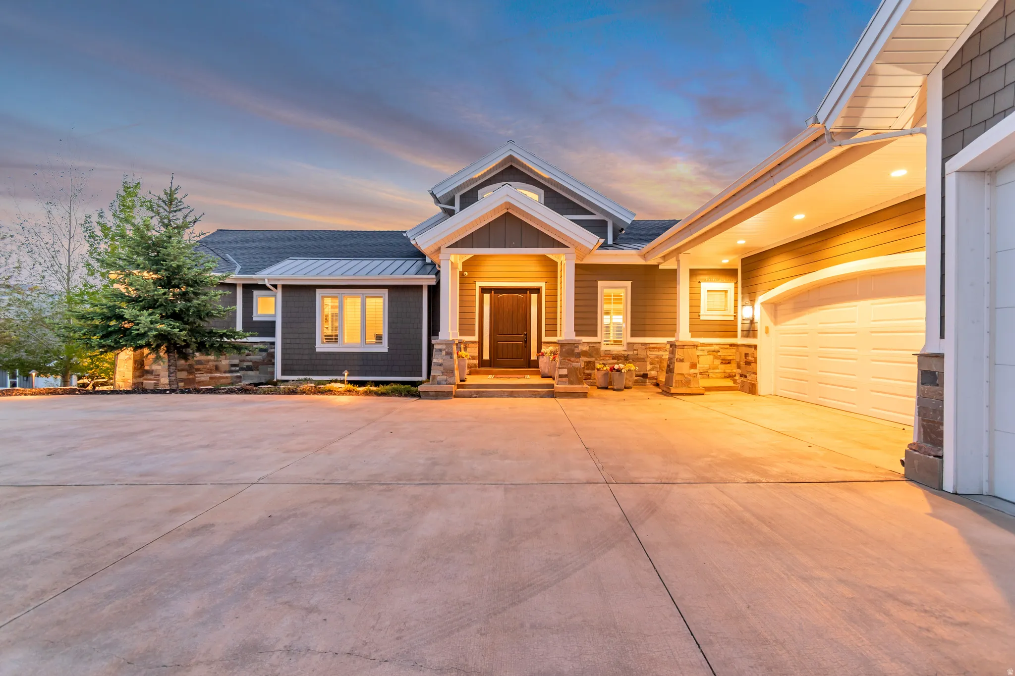 Contemporary exterior featuring dark gray siding, stone accents, multiple large windows, a covered entry, and an attached two-car garage with a concrete driveway