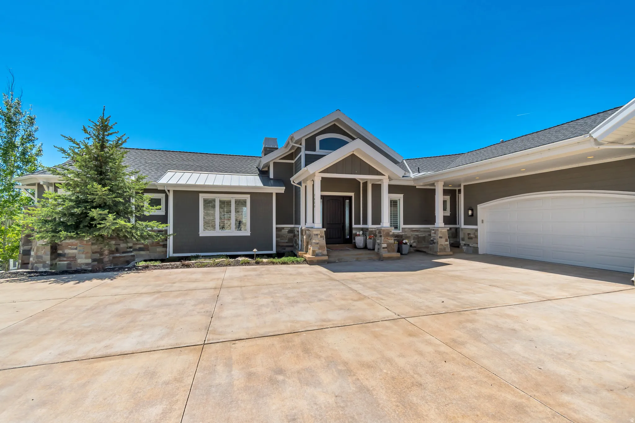 Contemporary exterior featuring dark siding, a prominent gabled entry, stone accents, a multi-pane window, and an attached garage with an arched door