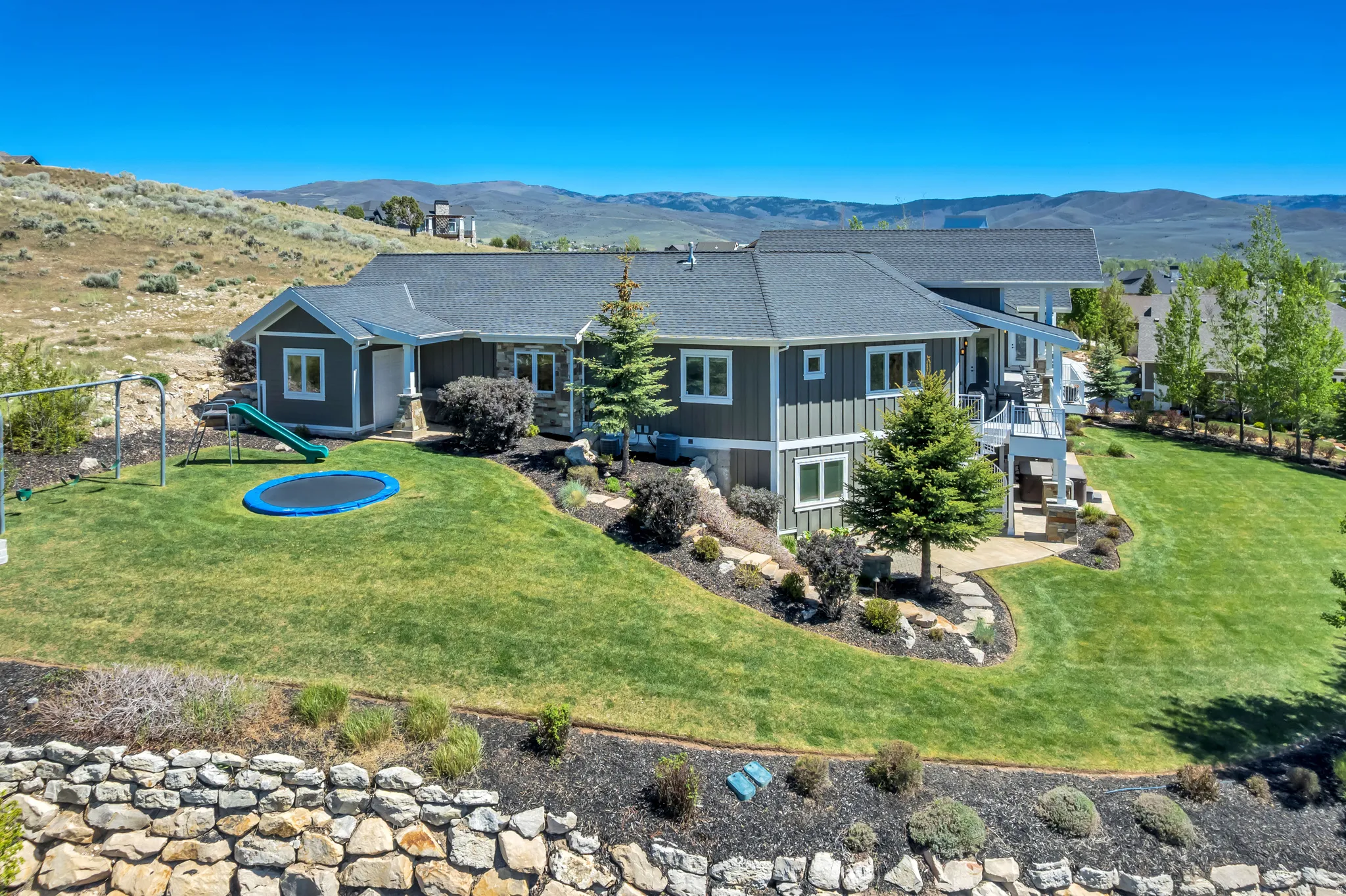 Expansive backyard featuring a manicured lawn, tiered landscaping, and a stone retaining wall