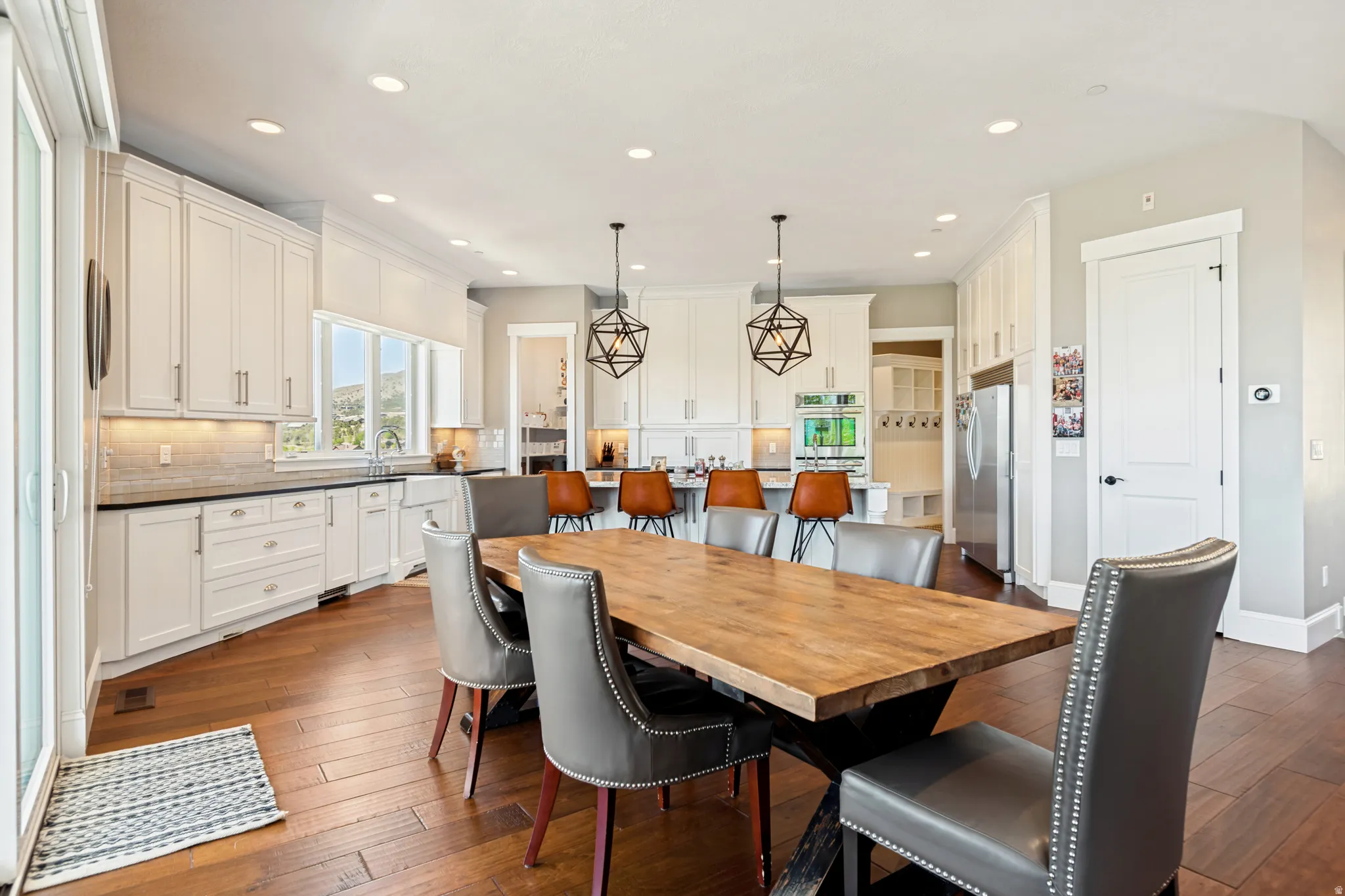 Open-concept kitchen and dining area featuring rich wood-finish flooring, white shaker cabinetry, stainless steel appliances, and recessed lighting