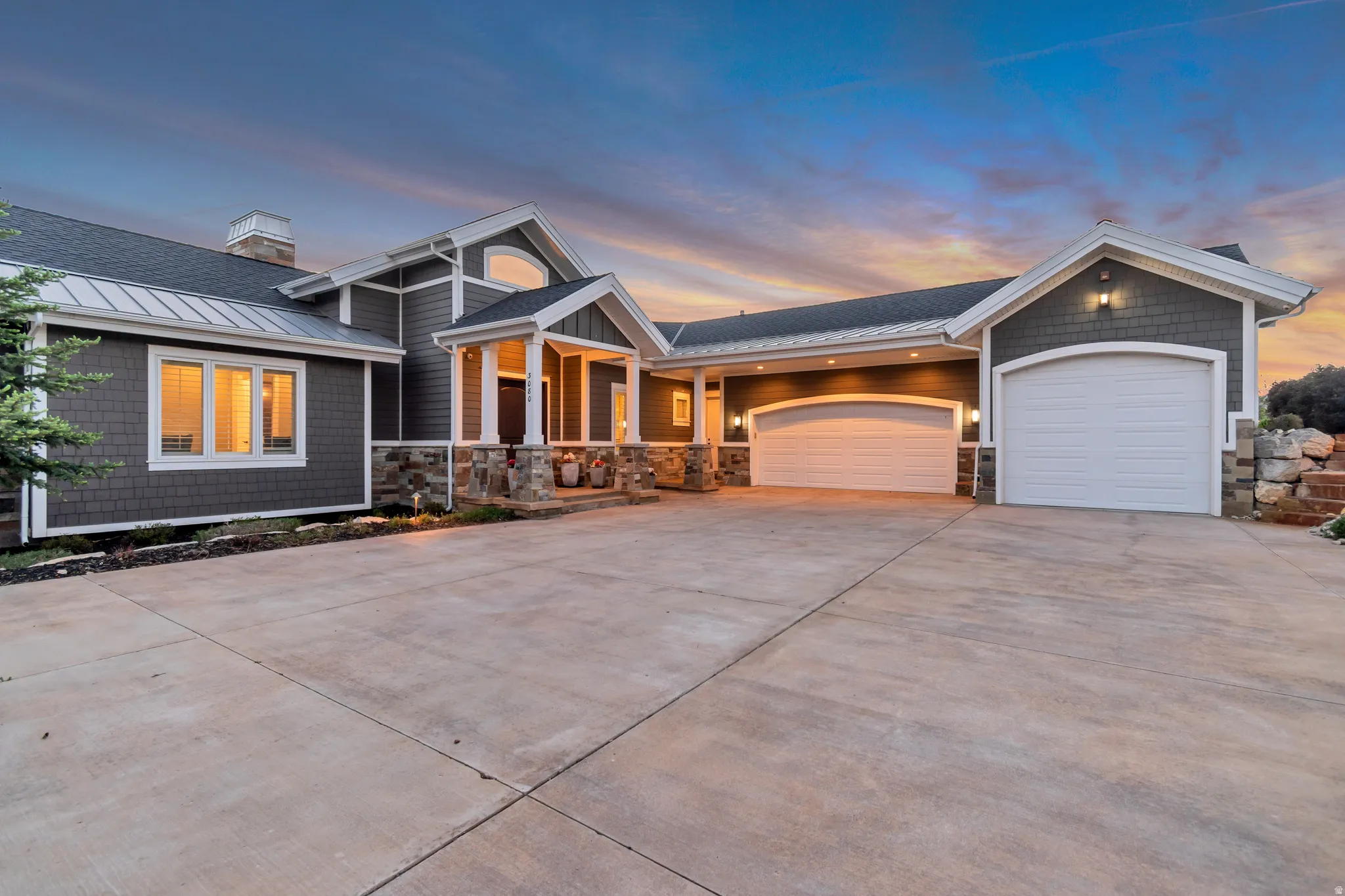 Contemporary home exterior featuring shake siding, stone accents, multiple garage bays with arched doors, a covered entry with columns, and a concrete driveway
