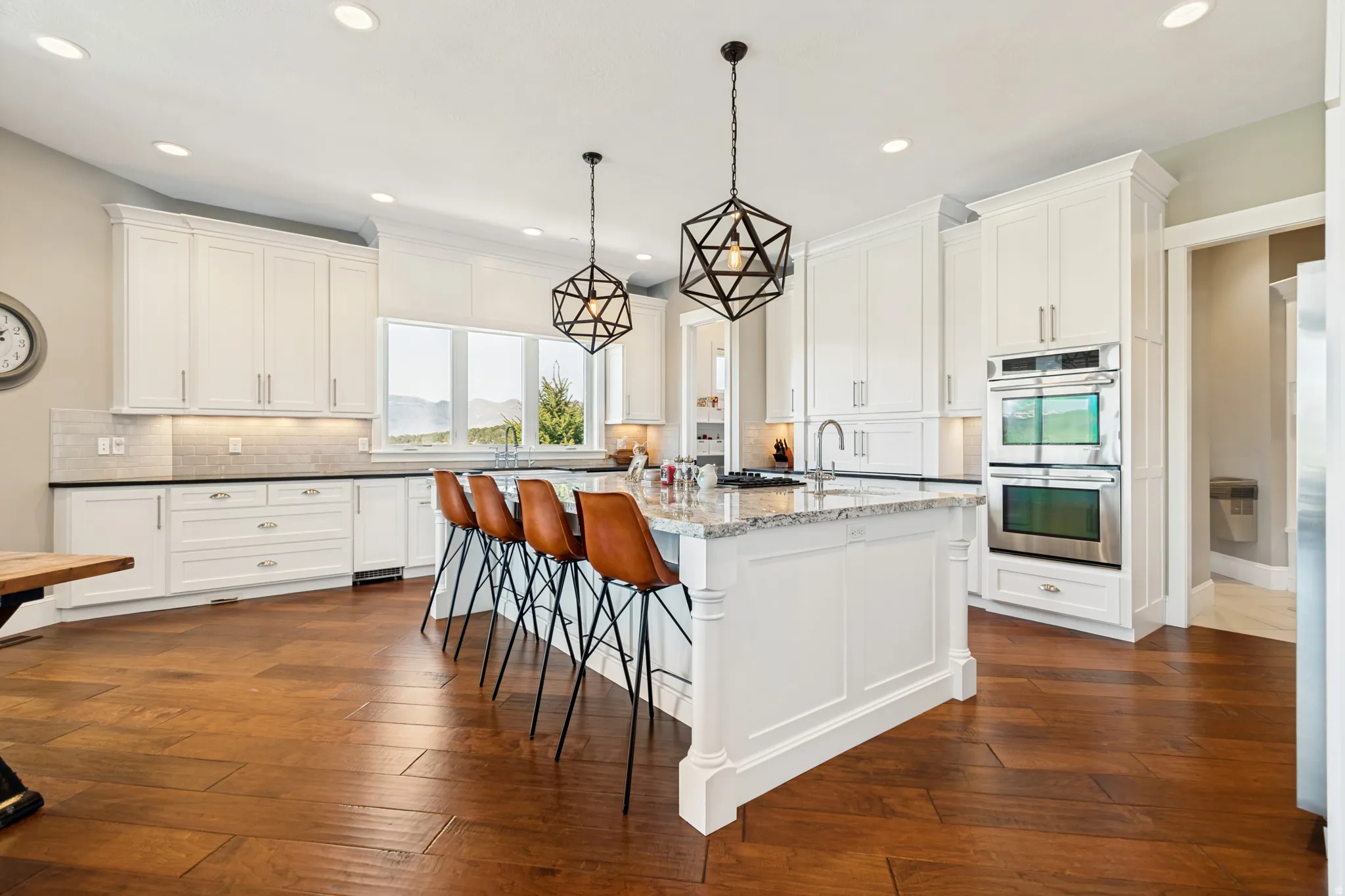 Gourmet kitchen featuring a large central island with seating, white shaker cabinetry, dark countertops, built-in double ovens, and wood-finish flooring
