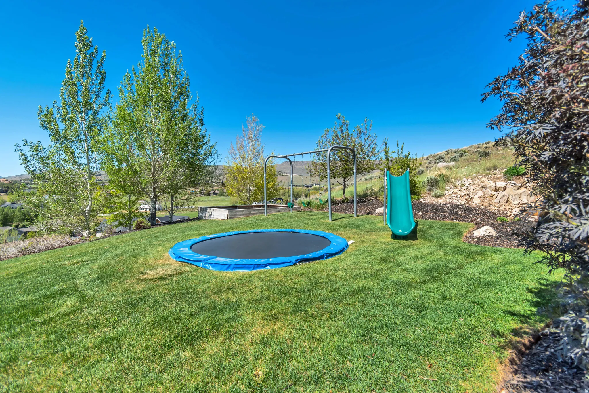 Expansive sloped backyard featuring established green lawn, mature trees, and natural rock landscaping