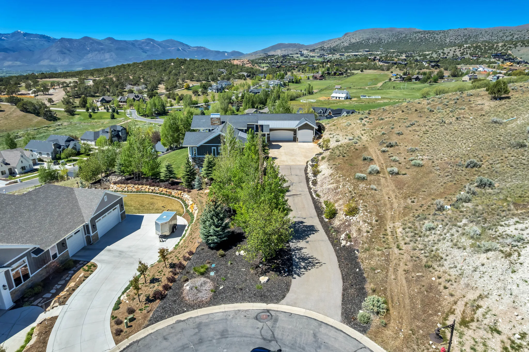 Expansive cul-de-sac property featuring a paved driveway, mature trees, and a terraced landscape