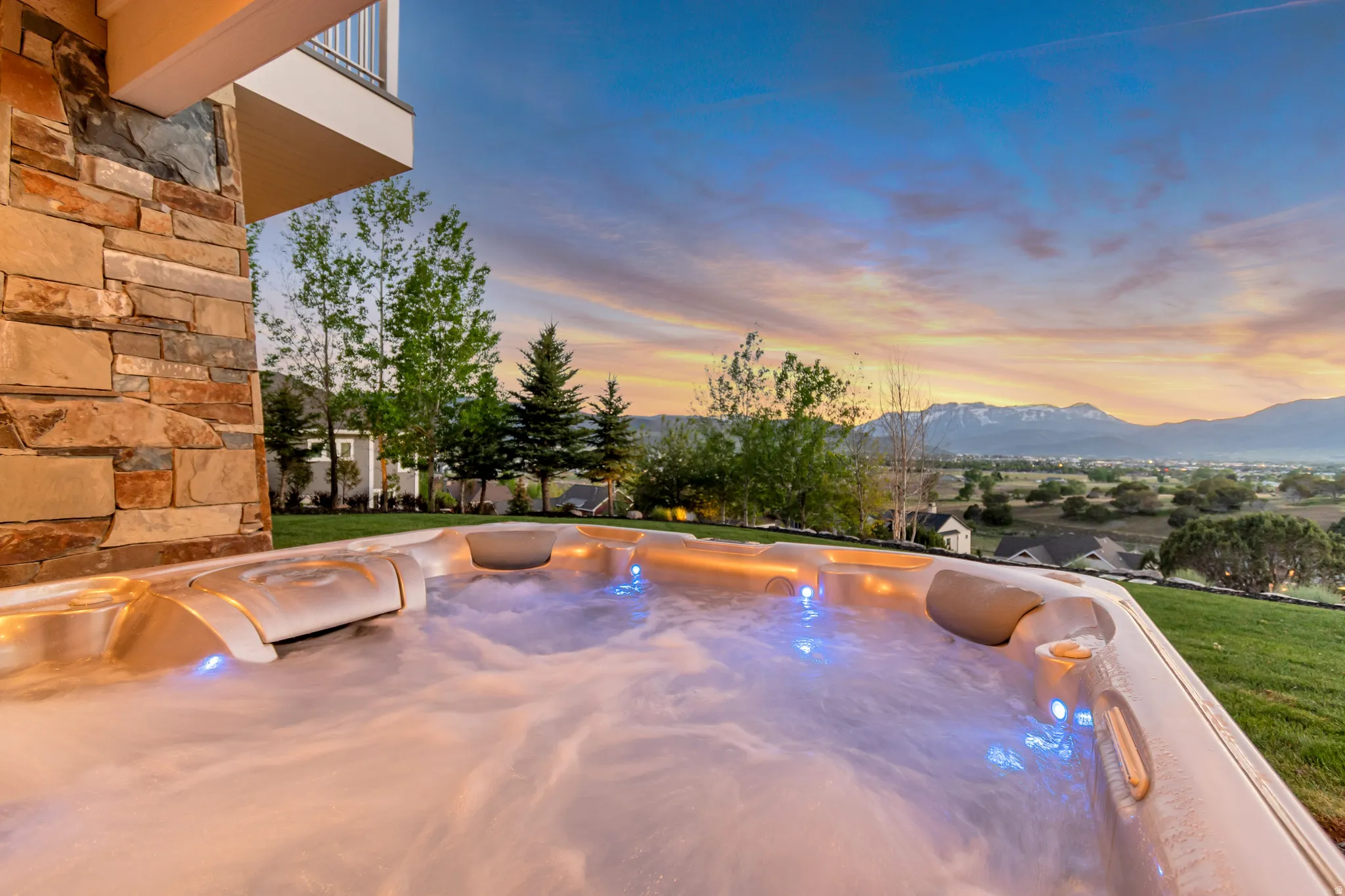 Integrated spa with blue accent lighting, surrounded by a manicured lawn and stone-clad exterior details