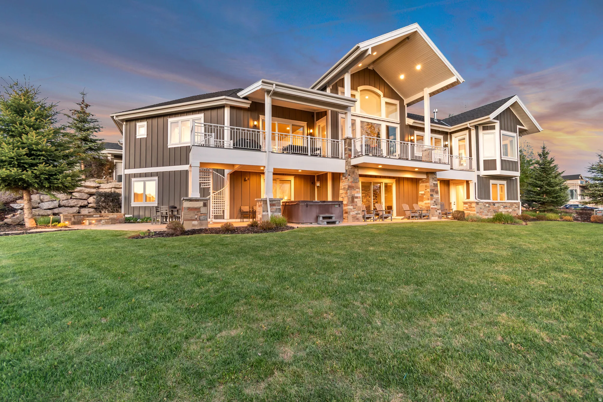 Expansive backyard with a manicured lawn, multi-level patio spaces, and mature evergreen trees