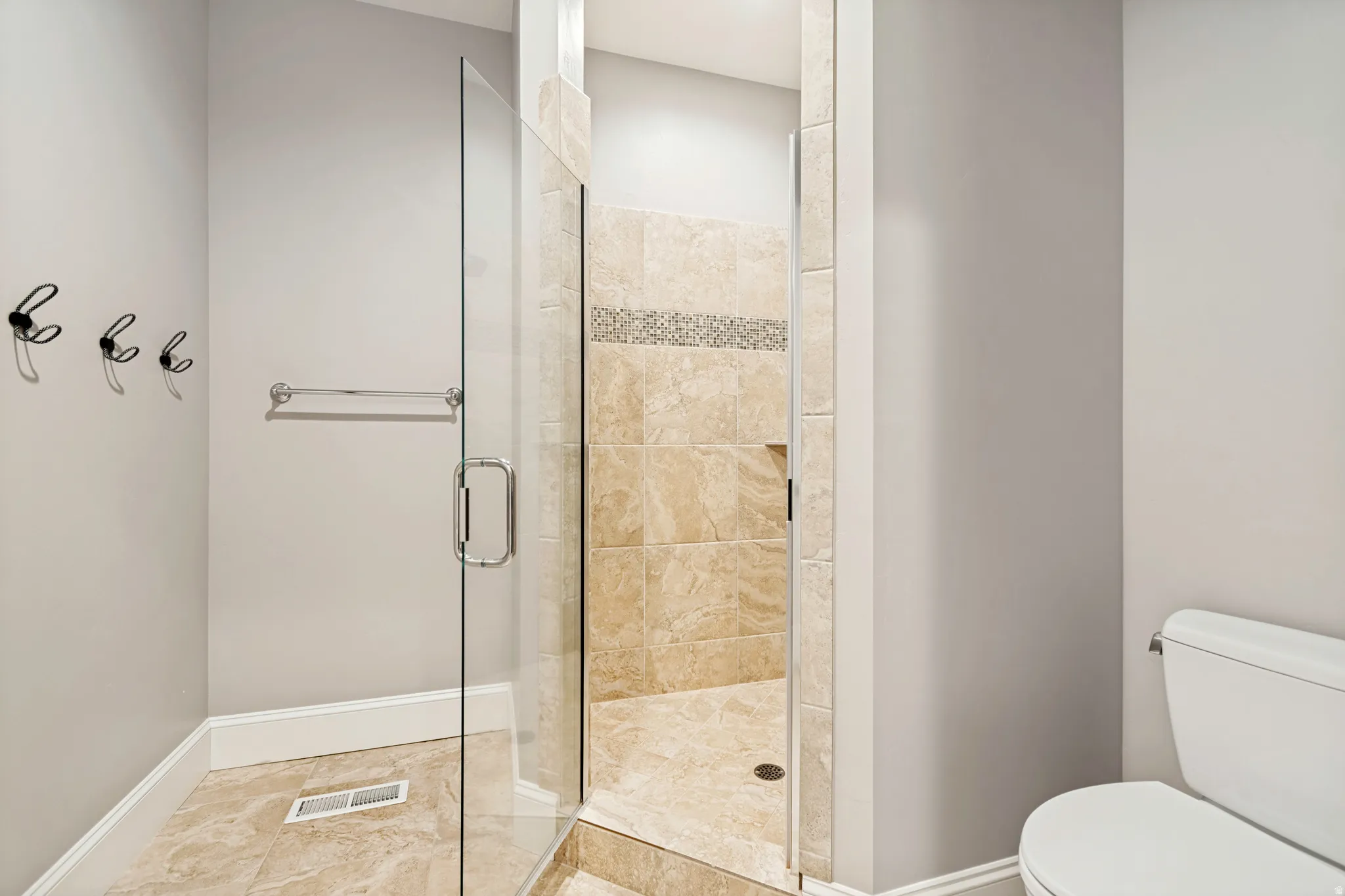 Glass-enclosed shower with full-height beige tile surround, decorative accent tile band, and built-in toiletry niche