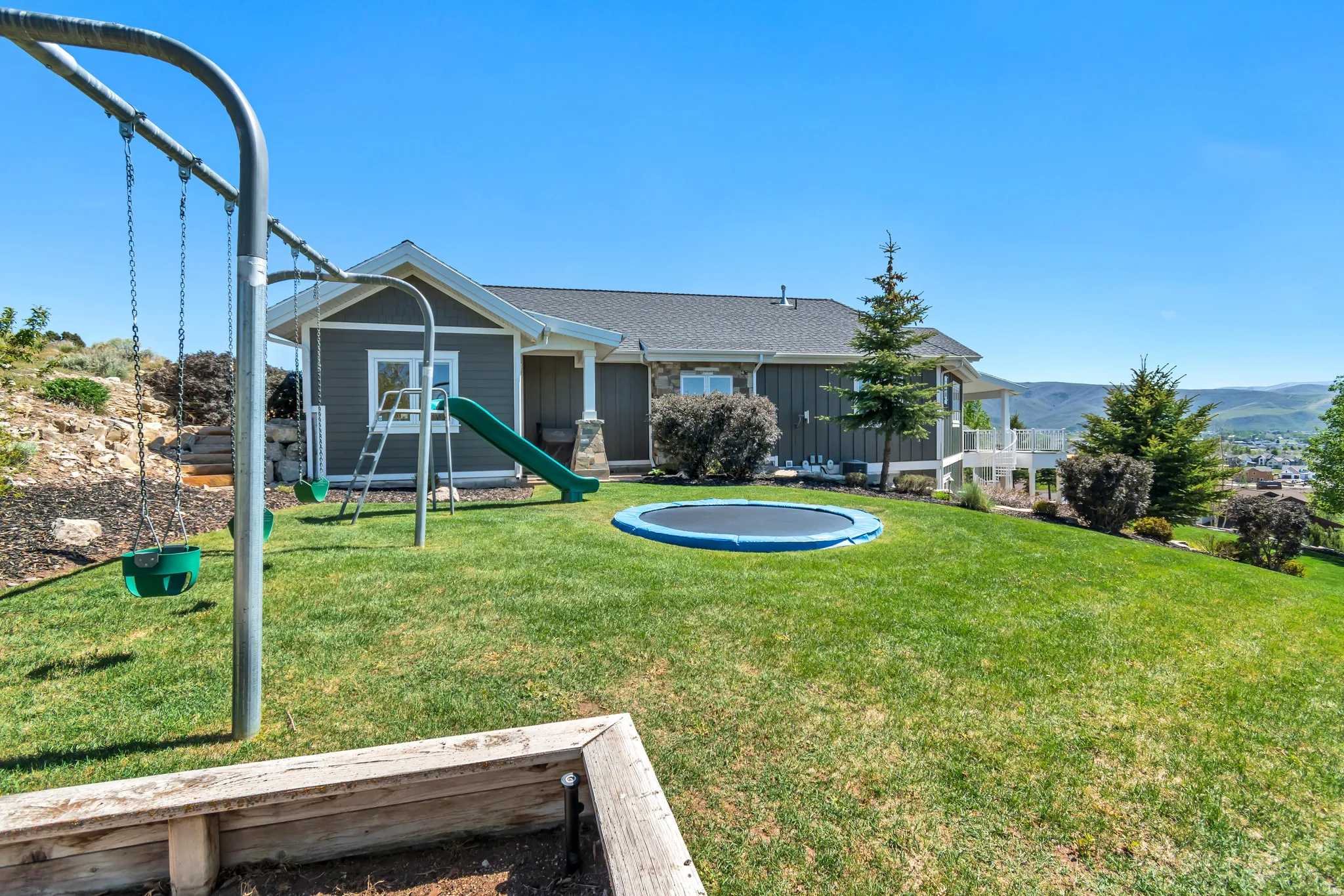 Expansive terraced backyard featuring a manicured lawn, established landscaping, and a white deck with railings overlooking the distant landscape