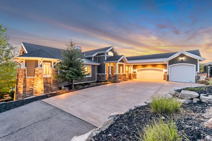 Multi-level residence featuring gray siding with white trim, stone veneer accents, an attached three-car garage, and a concrete driveway