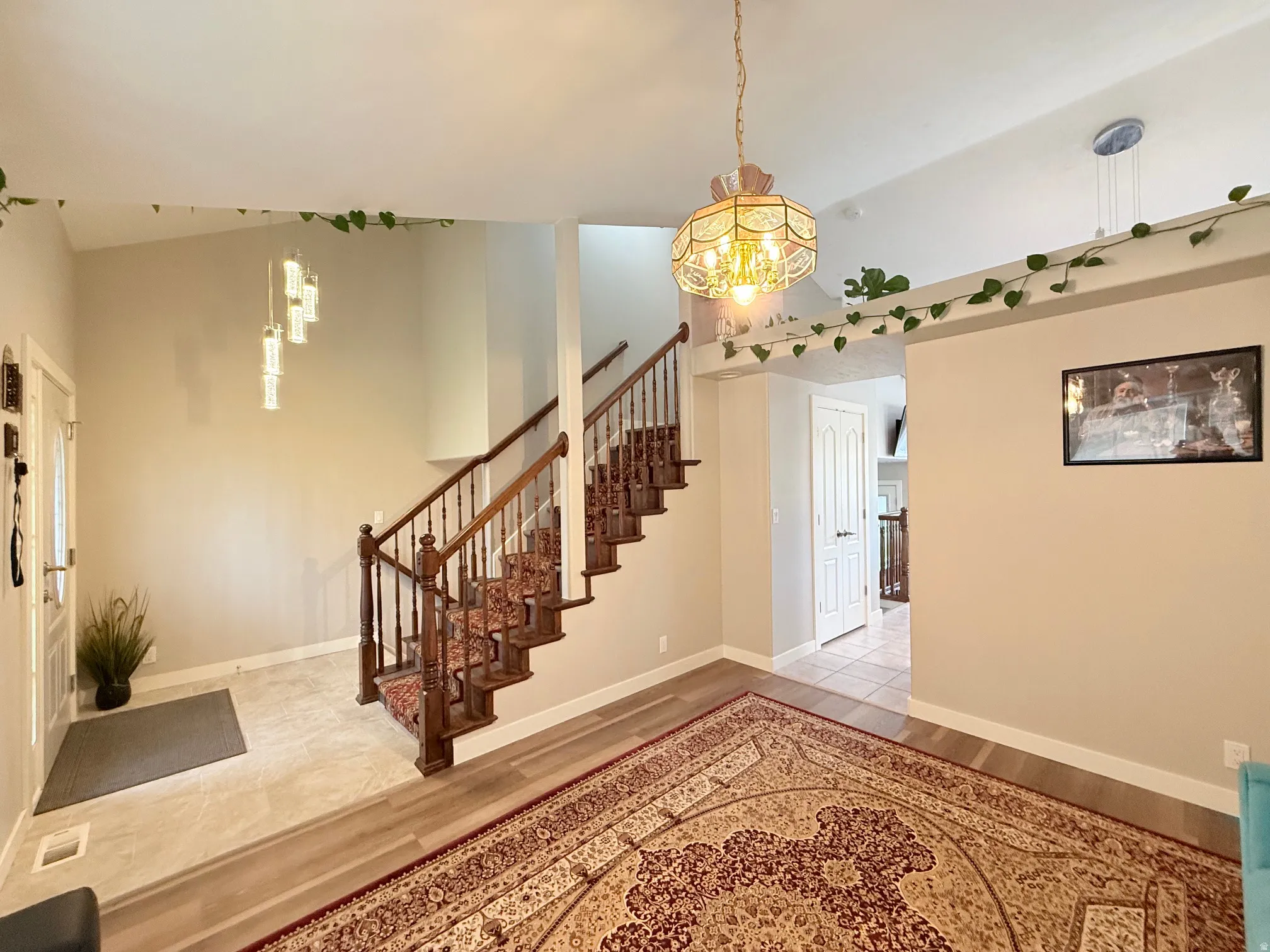 Foyer with a grand staircase featuring wood balusters and a carpet runner, complemented by wood-finish flooring and a tiled entry