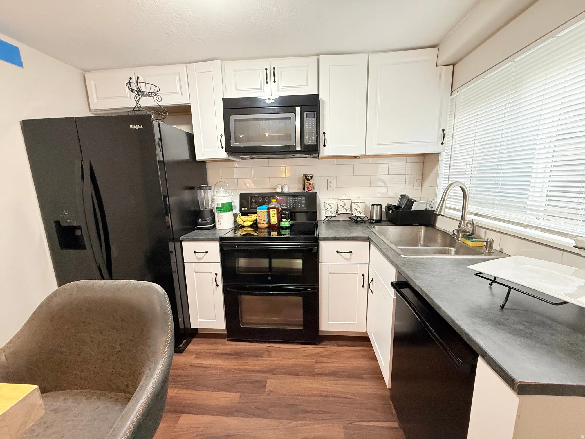 Kitchen featuring white cabinetry, dark countertops, wood-finish flooring, a stainless steel sink with a gooseneck faucet, and a subway tile backsplash