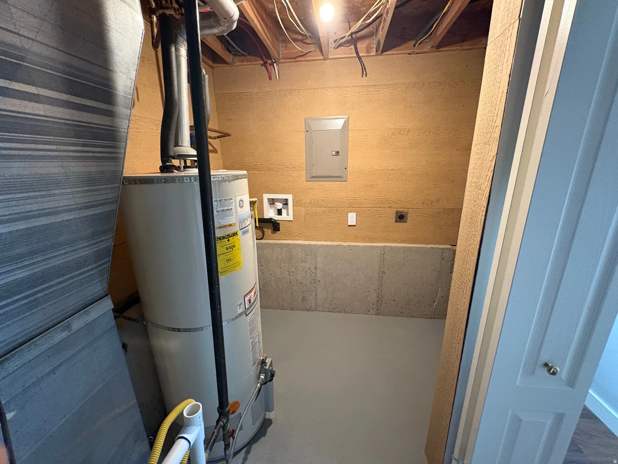 Basement utility area featuring a water heater, exposed ceiling joists, and a circuit breaker panel