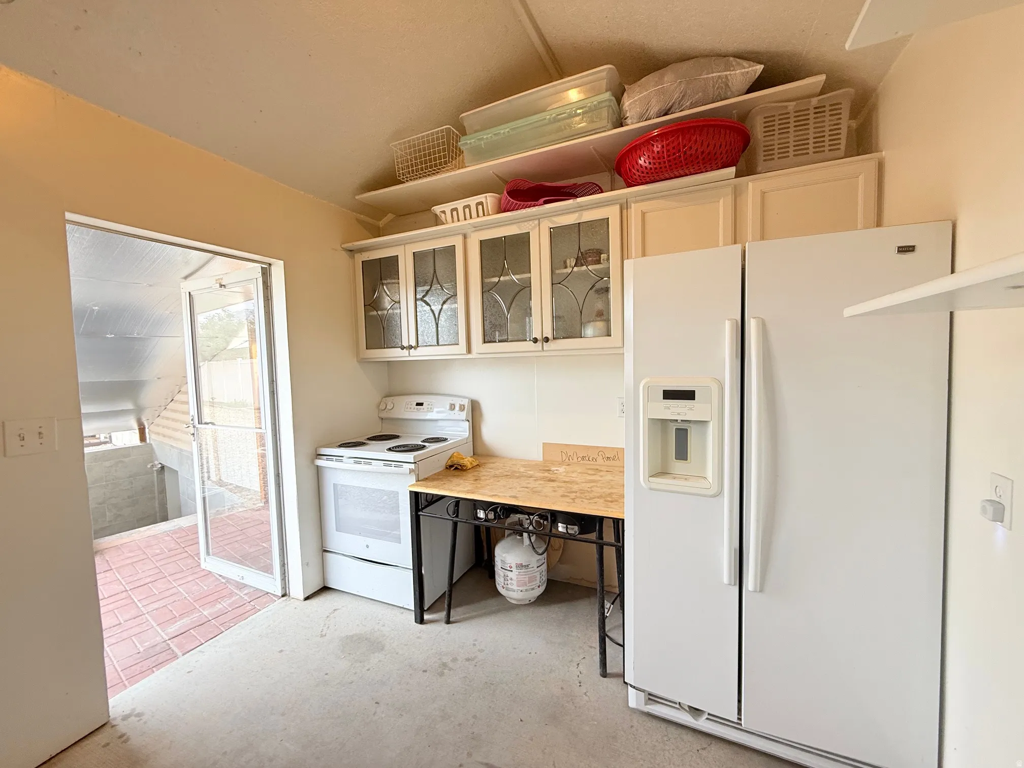 Kitchen area featuring white cabinetry with glass-front upper doors, white appliances, and a red brick paver patio accessible through a glass screen door