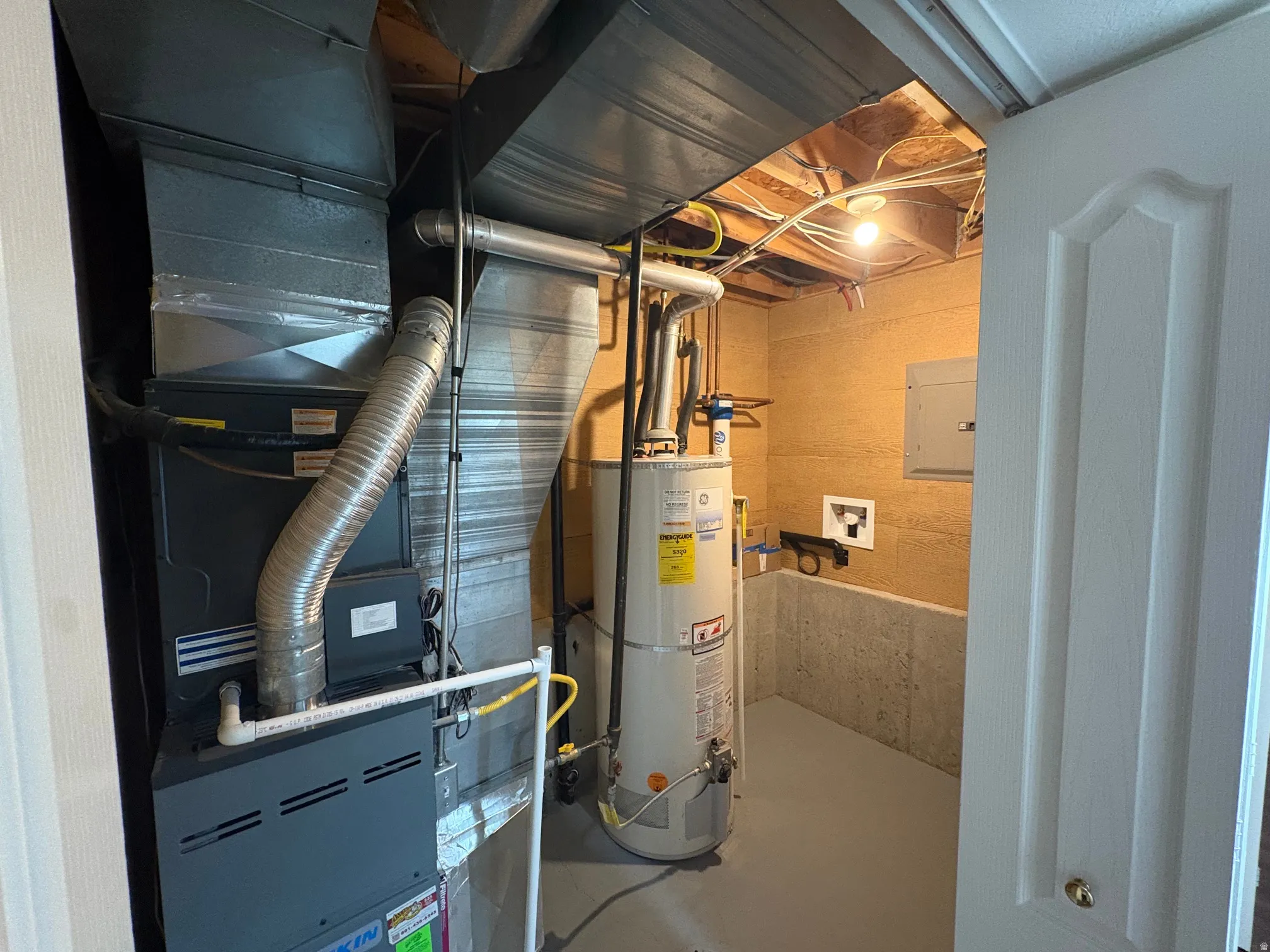 Utility room featuring a furnace unit, water heater, electrical panel, and exposed ceiling joists