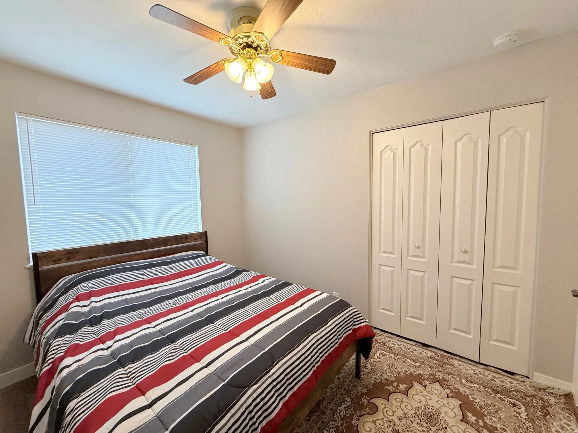 Room featuring a window with blinds, ceiling fan with light kit, and bi-fold closet doors