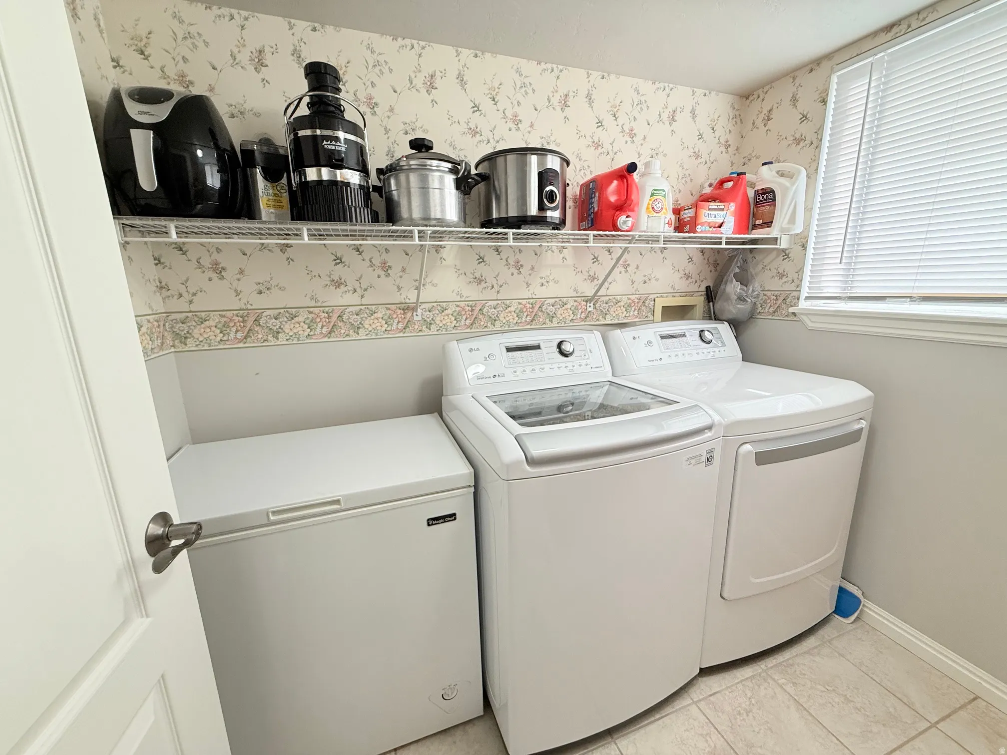 Utility room featuring a window with blinds, upper wire shelving, and light-toned tile flooring