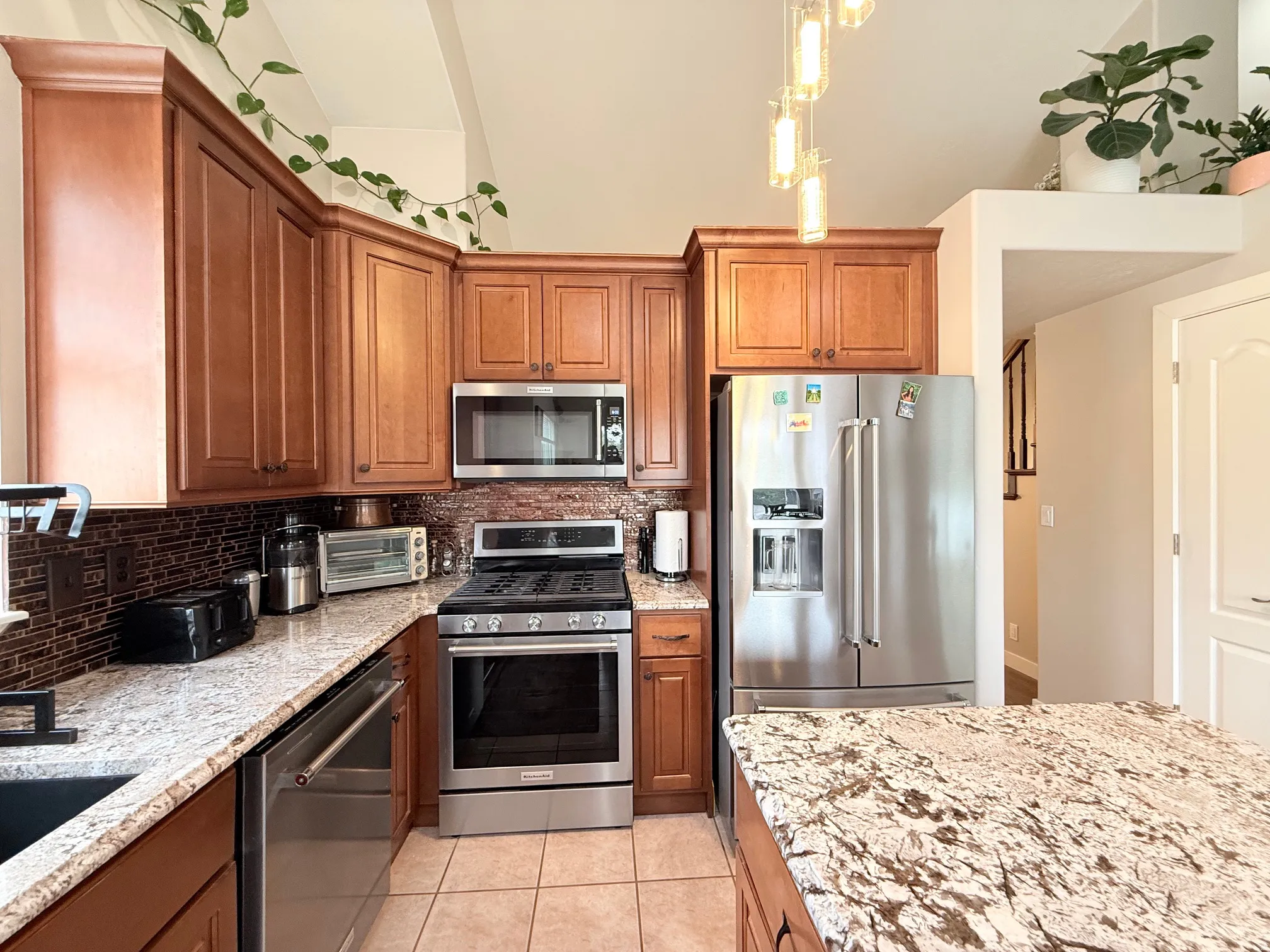 Kitchen featuring wood cabinetry, stainless steel appliances, speckled stone countertops, a tiled backsplash, and recessed lighting