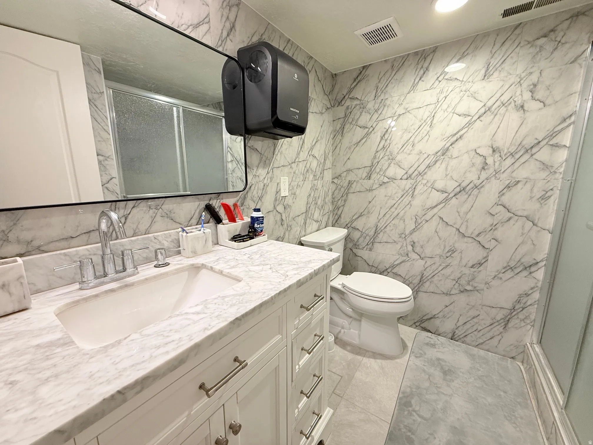 Bathroom featuring a white vanity with a rectangular undermount sink, a marble-patterned countertop, and full-height marble-patterned wall panels