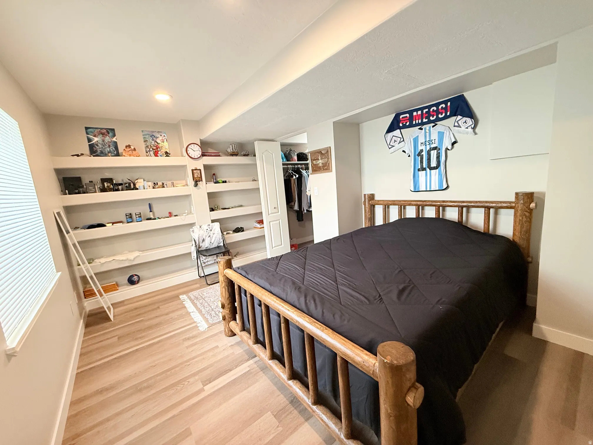 Light wood-finish flooring featuring a window with blinds, recessed ceiling lighting, and built-in shelving