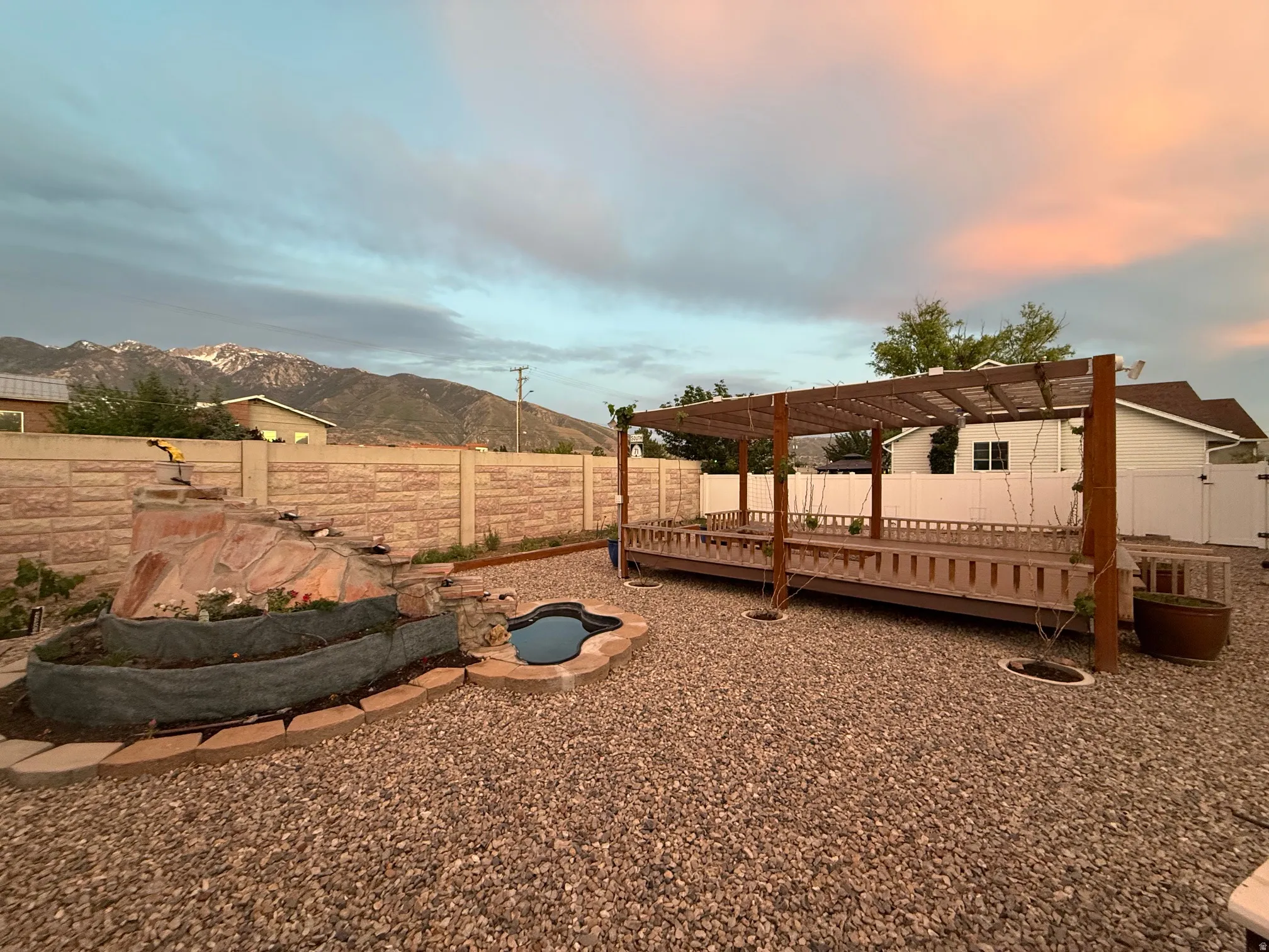 Expansive outdoor area featuring a pergola-covered deck, a rock water feature with an integrated pond, and gravel ground cover