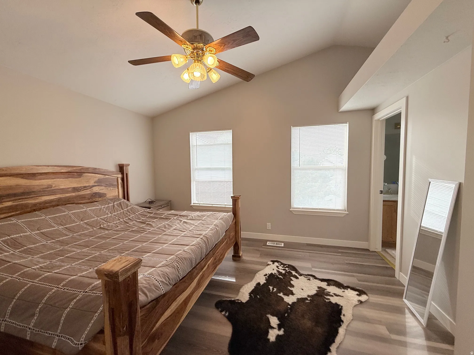 Vaulted ceiling bedroom featuring a ceiling fan with integrated lighting, two windows with blinds, and wood-finish flooring