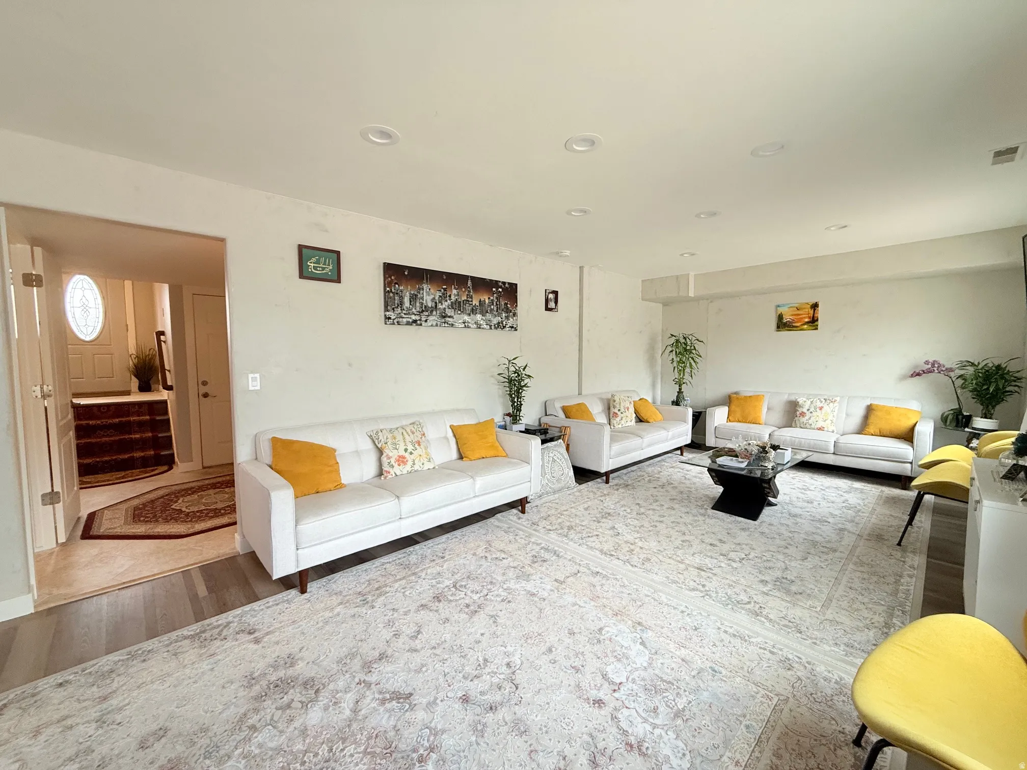Spacious living area featuring light-toned walls, recessed lighting, and wood-finish flooring extending into the entry