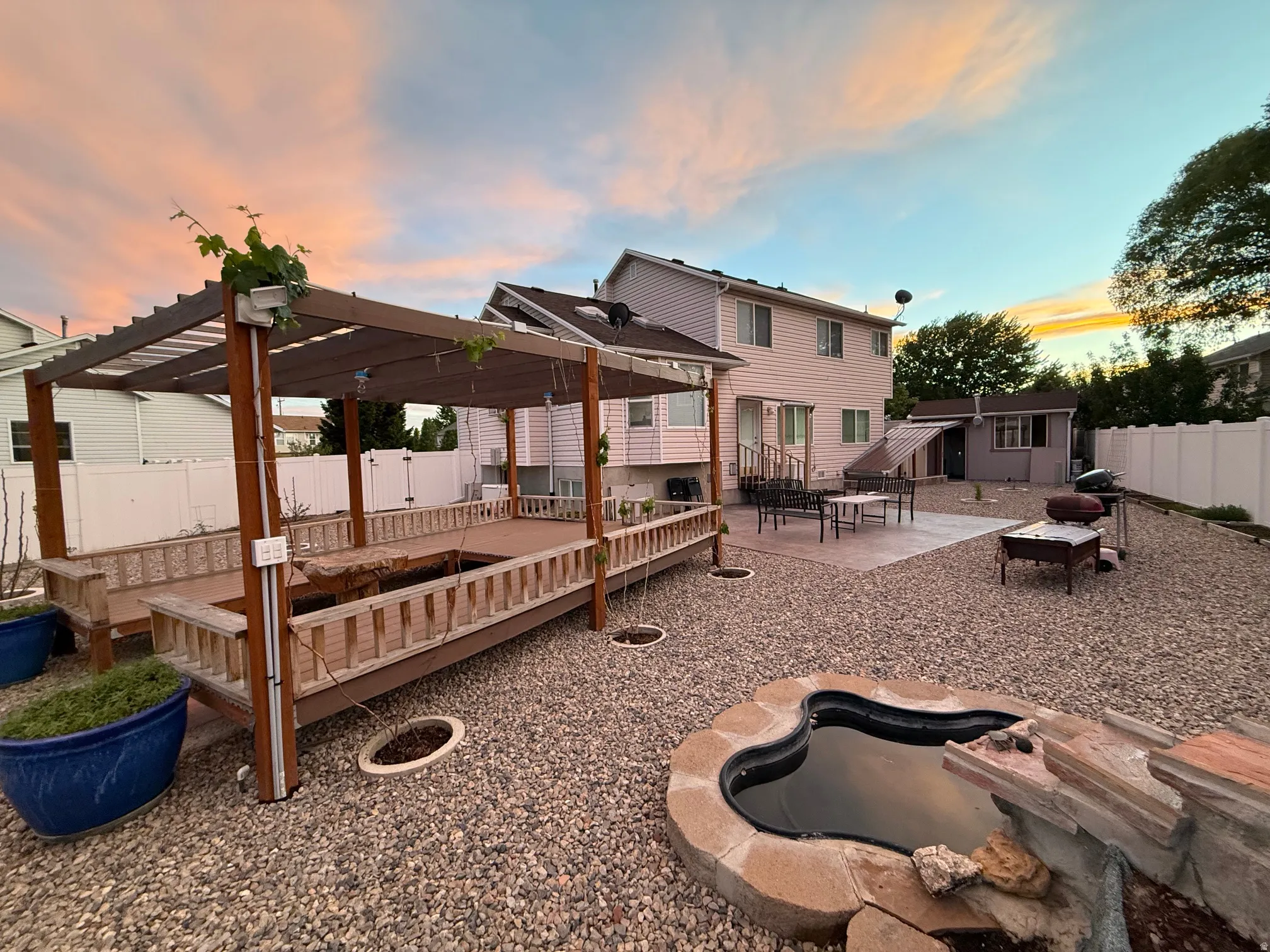 Expansive backyard featuring a pergola-covered deck with integrated seating, a paved patio area, and a dedicated storage shed