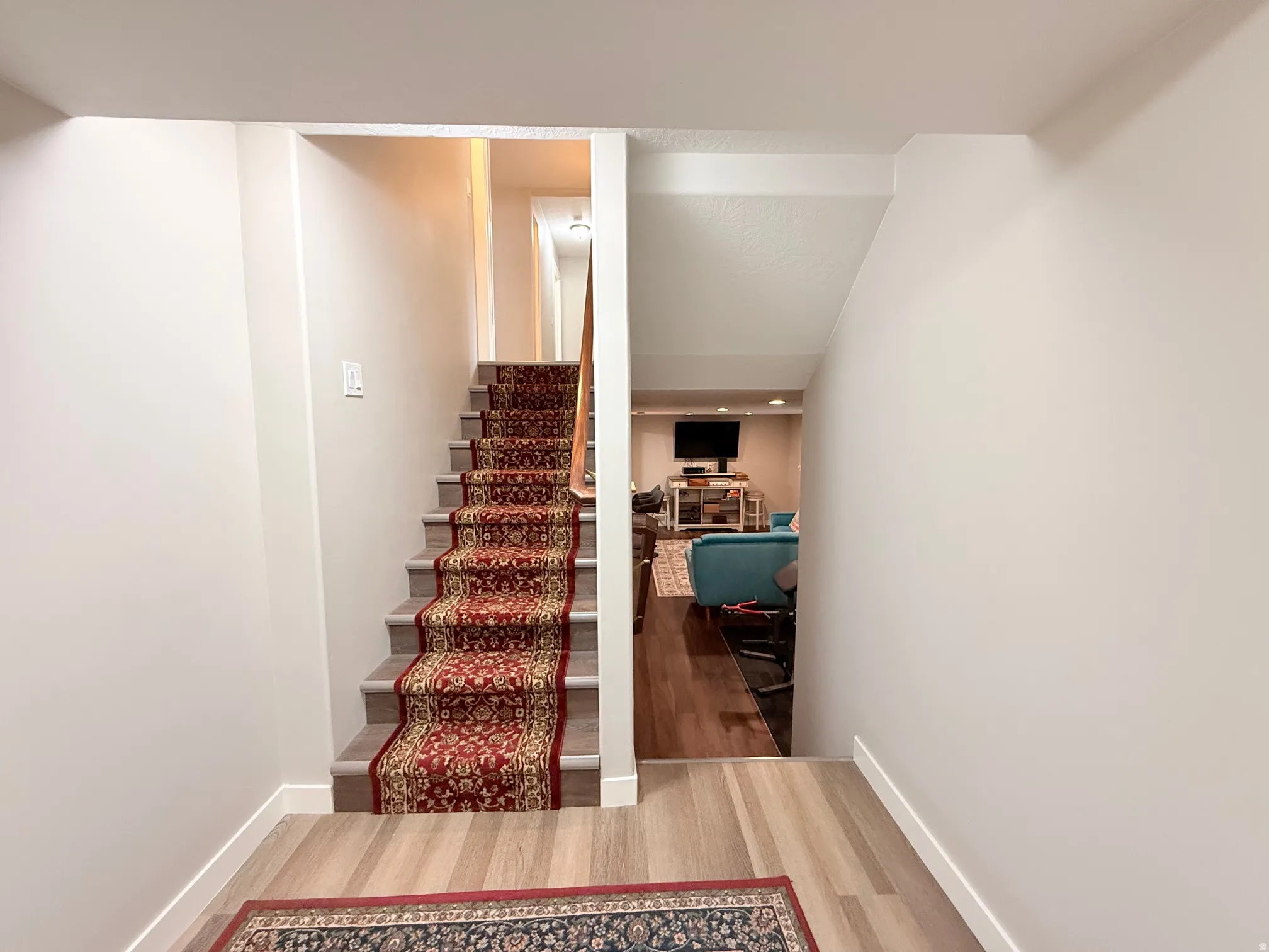 Staircase featuring a patterned red and gold runner, light gray risers, and a wooden handrail