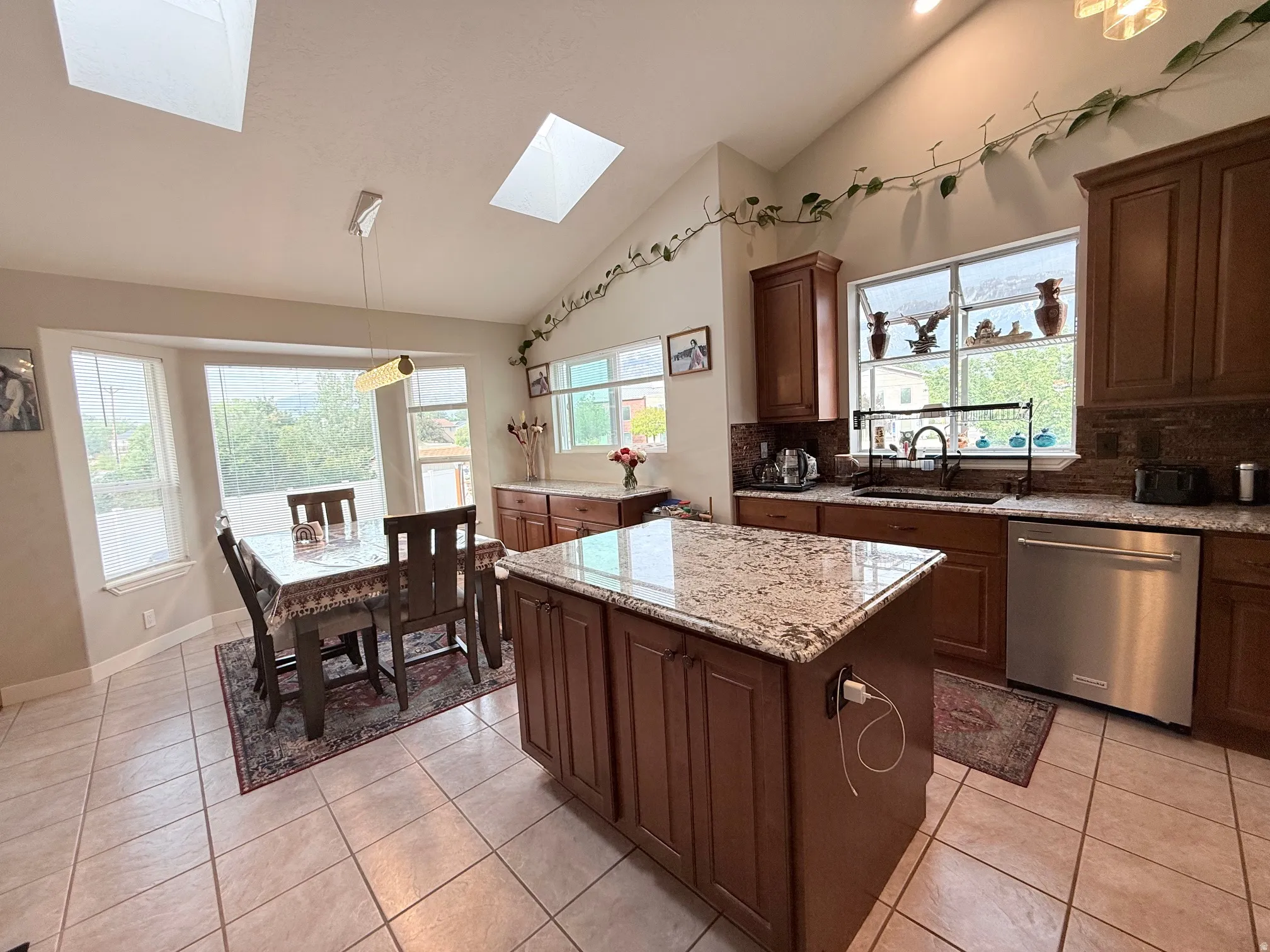 Kitchen and dining area featuring a central island with a granite countertop, wood-finish cabinetry, tile flooring, and multiple skylights