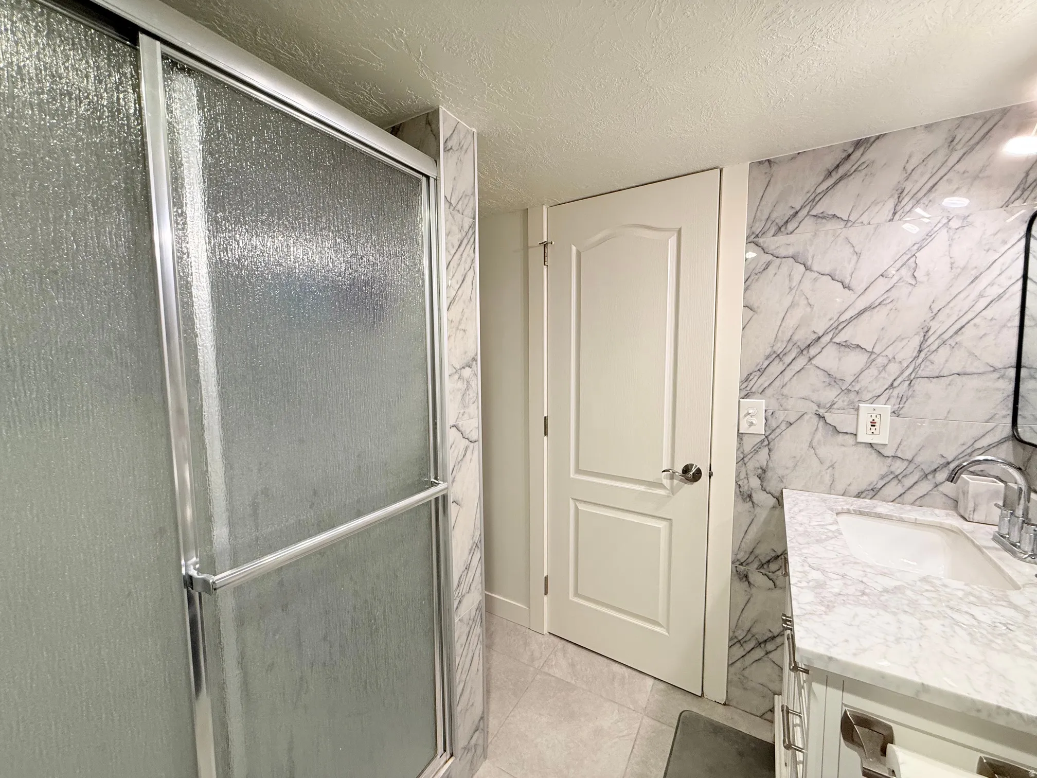 Bathroom featuring a glass-enclosed shower, white vanity with integrated sink, and a mirrored accent wall