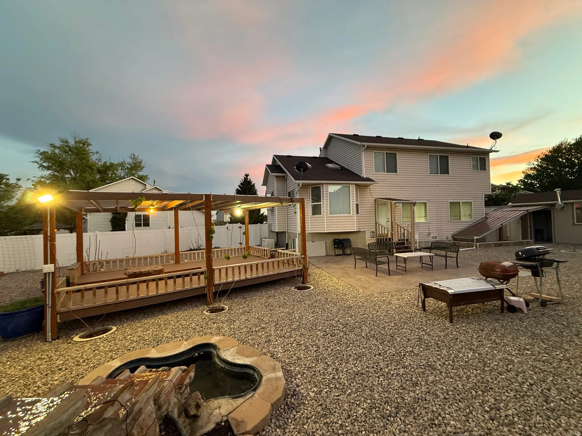 Expansive outdoor living area featuring a gravel ground cover, a large raised wooden deck with a pergola, and a decorative water feature