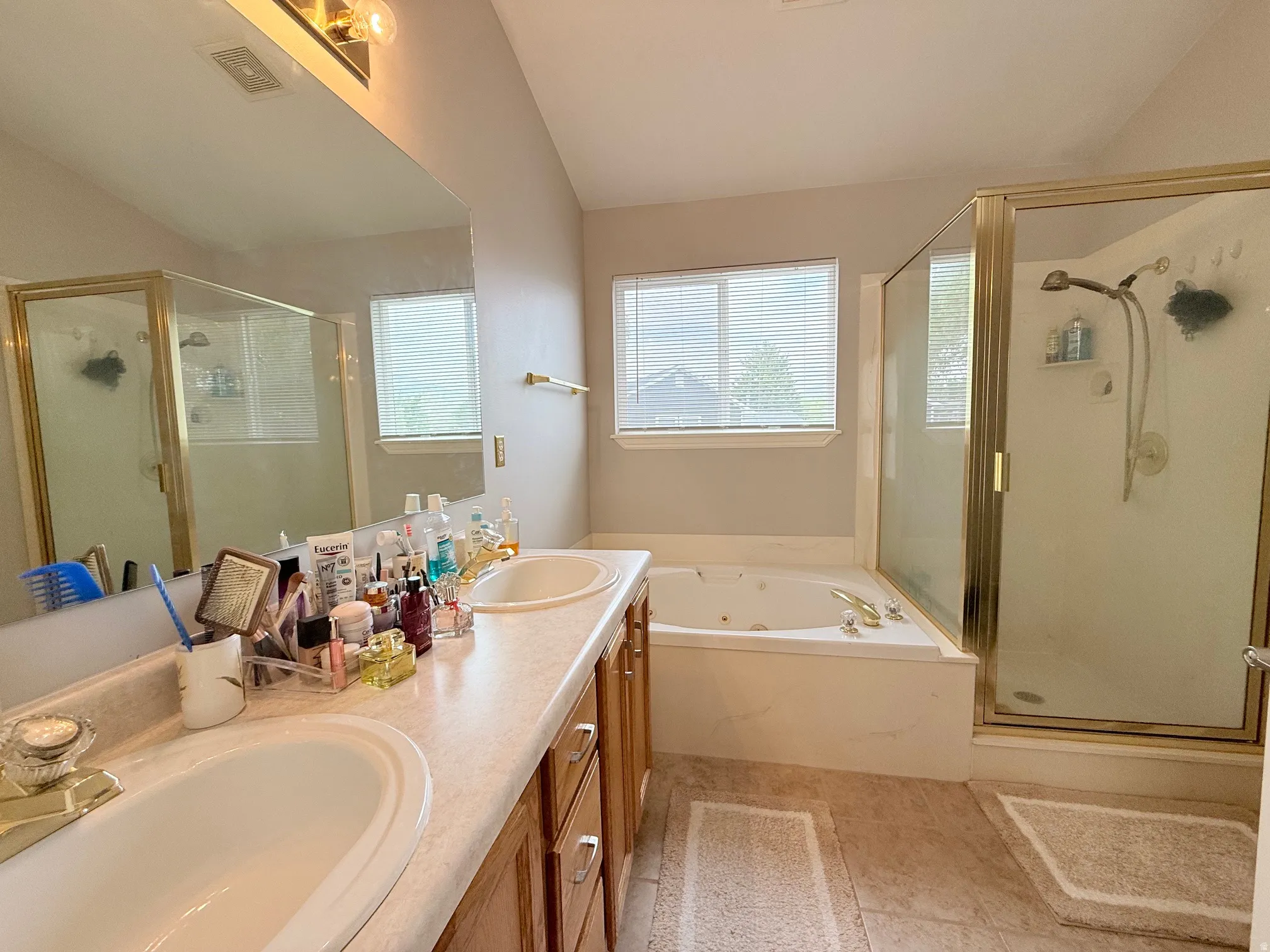 Bathroom featuring a dual vanity with integrated sinks, a built-in jetted tub, a separate shower with a glass enclosure, light wood-finish cabinetry, and tiled flooring