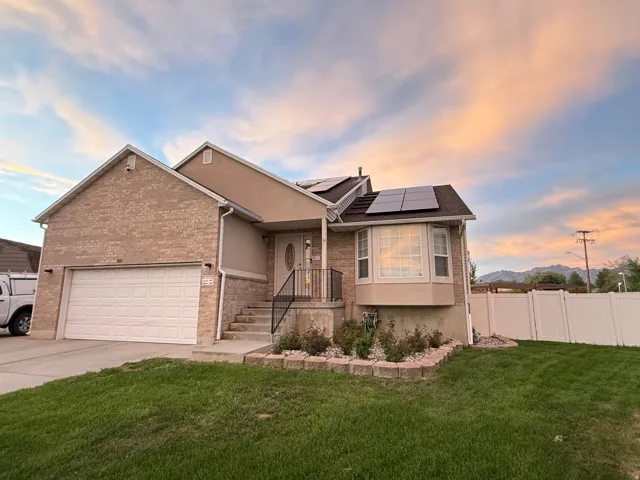 Brick and stucco exterior featuring a two-car garage, front entry with a bay window, and rooftop solar panels