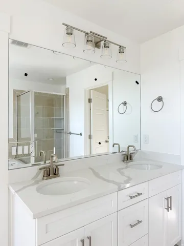 Dual vanity featuring white shaker-style cabinetry, a stone-finish countertop with integrated sinks, and brushed nickel hardware
