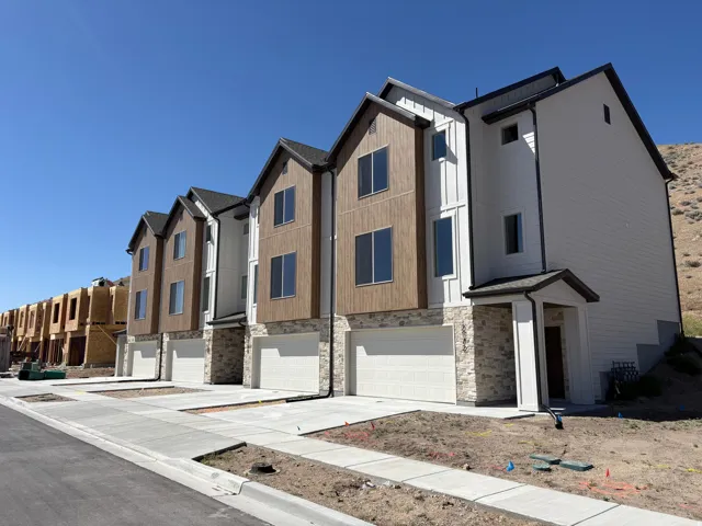 Contemporary townhome exterior featuring white siding, brown vertical siding accents, stone veneer finishes, dark-framed windows, and an attached two-car garage
