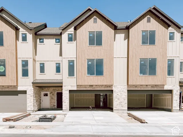 Multi-level exterior featuring vertical board-and-batten siding, stone masonry veneer, pitched rooflines, and multiple attached garage bays
