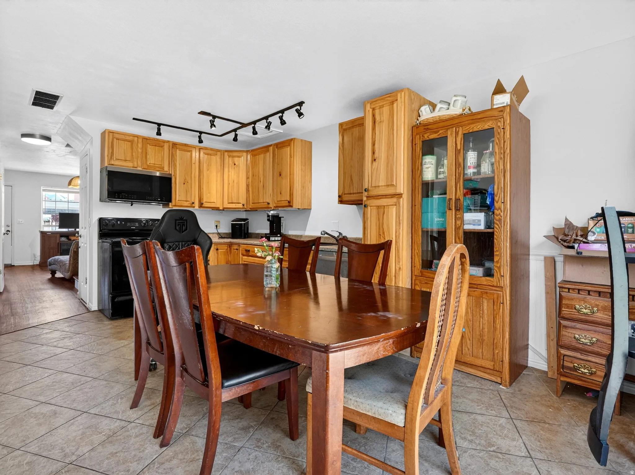 Kitchen and dining area featuring light wood cabinetry, black appliances, track lighting, and tile flooring