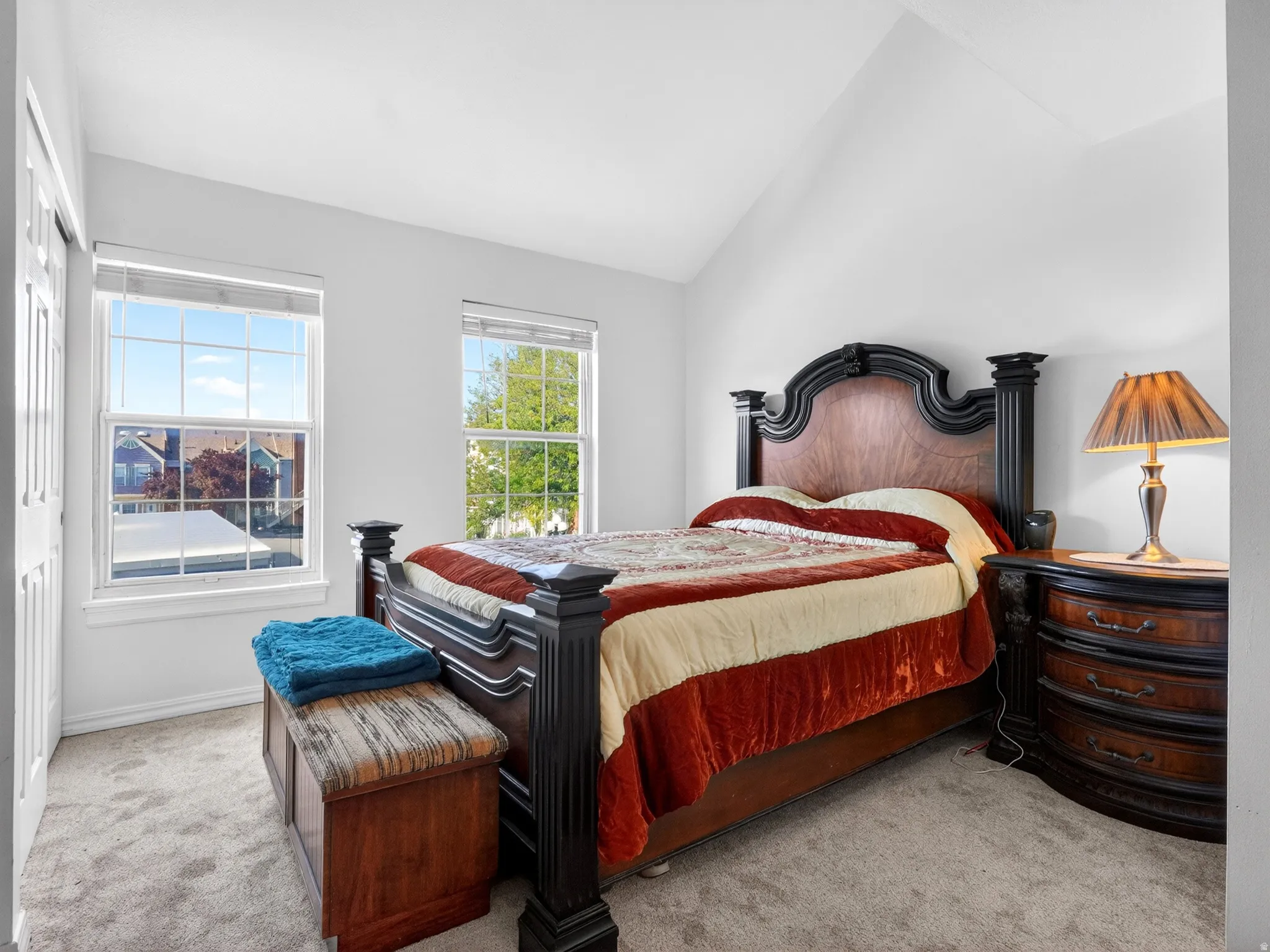 Bright bedroom featuring two large windows, vaulted ceiling, plush carpet, and white bi-fold closet doors