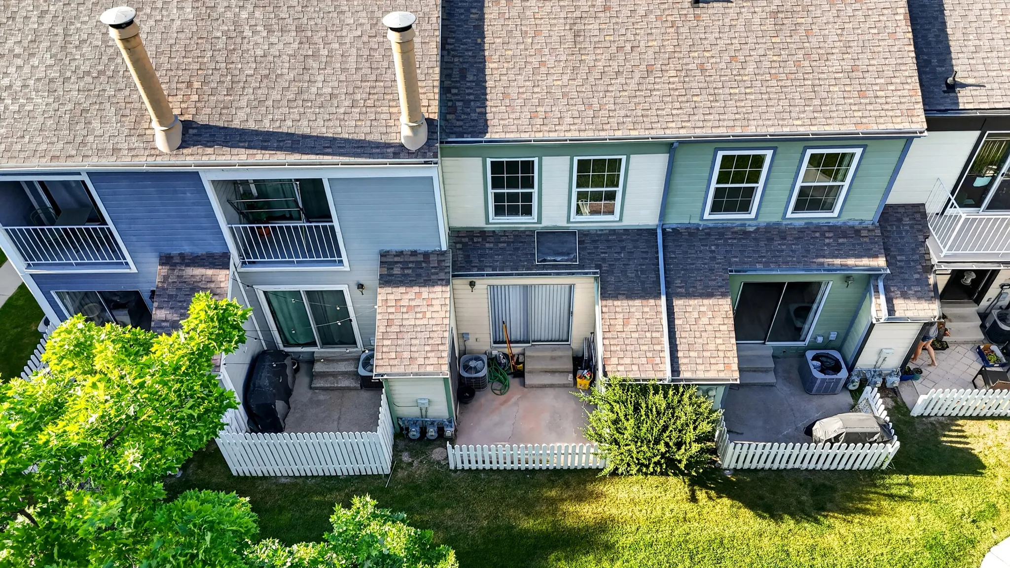 Rear exterior of townhome featuring private fenced patios, sliding glass doors, white picket fencing, and a shingle roof