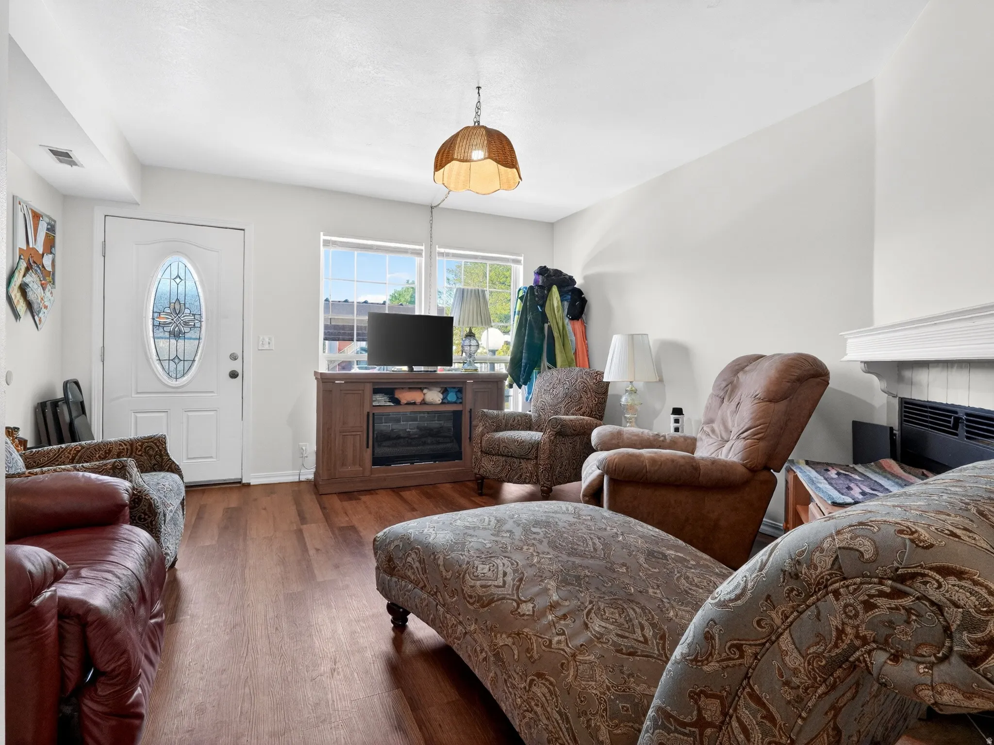 Living space featuring wood-finish flooring, a white entry door with decorative glass, two windows, a built-in electric fireplace, and a light-toned ceiling
