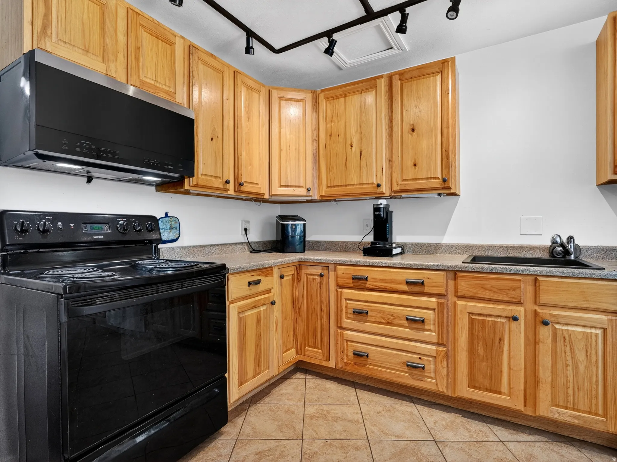 Full kitchen featuring abundant wood cabinetry, integrated black appliances, a track lighting system, and a double-basin sink